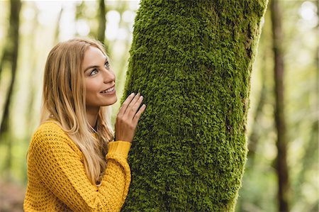 simsearch:6109-08481688,k - Beautiful blonde woman standing next to a tree trunk in the woods Photographie de stock - Premium Libres de Droits, Code: 6109-08481697