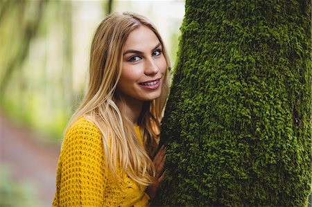 simsearch:6109-08481684,k - Beautiful blonde woman standing next to a tree trunk in the woods Foto de stock - Sin royalties Premium, Código: 6109-08481695