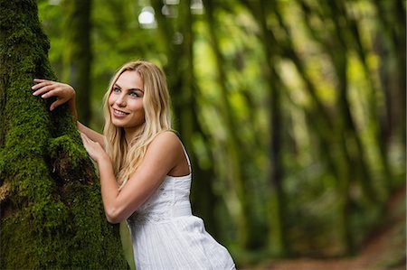 simsearch:6109-08481684,k - Beautiful blonde woman standing next to a tree trunk in the woods Foto de stock - Sin royalties Premium, Código: 6109-08481731