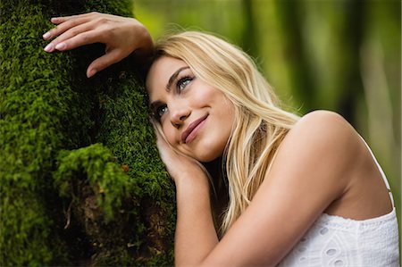 simsearch:6109-08481688,k - Beautiful blonde woman standing next to a tree trunk in the woods Photographie de stock - Premium Libres de Droits, Code: 6109-08481732
