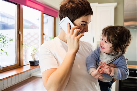 simsearch:6109-08390041,k - Cute mother on the phone and holding baby in the kitchen Stock Photo - Premium Royalty-Free, Code: 6109-08481811