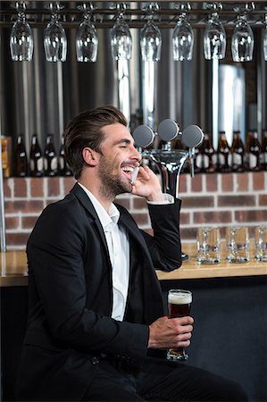 Handsome businessman holding a pint and calling in a pub Stock Photo - Premium Royalty-Free, Code: 6109-08489719