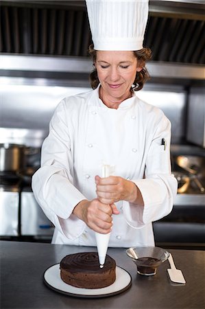 Chef piping icing on cake in a commercial kitchen Stock Photo - Premium Royalty-Free, Code: 6109-08489819