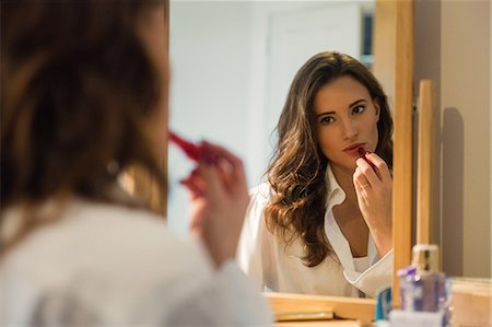 Beautiful brunette applying lipstick in front of the mirror at home Stock Photo - Premium Royalty-Free, Code: 6109-08435535