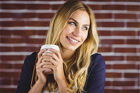 Beautiful woman holding takeaway cup of coffee against brick wall Stock Photo - Premium Royalty-Free, Code: 6109-08435711