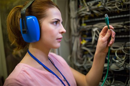 Technician in head phones looking at patch cable in server room Photographie de stock - Premium Libres de Droits, Code: 6109-08690138