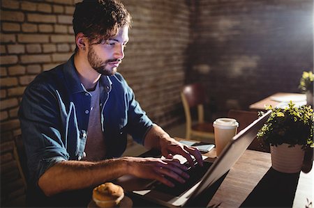 Young man concentrating on laptop with coffee and cupcake while sitting at cafe Foto de stock - Sin royalties Premium, Código: 6109-08690407