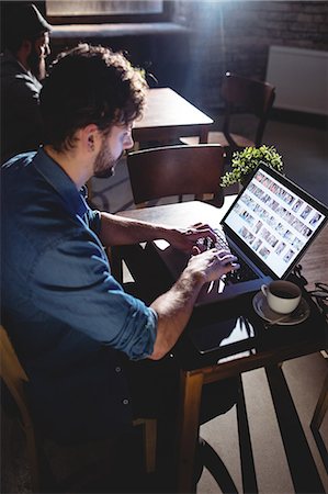 Side view of young man typing on laptop at coffee shop Stock Photo - Premium Royalty-Free, Code: 6109-08690416