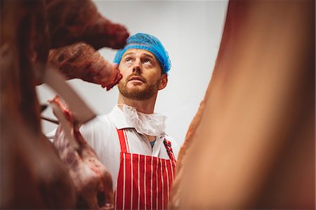 Butcher looking at the red meat hanging in storage room at butchers shop Stock Photo - Premium Royalty-Free, Code: 6109-08764516