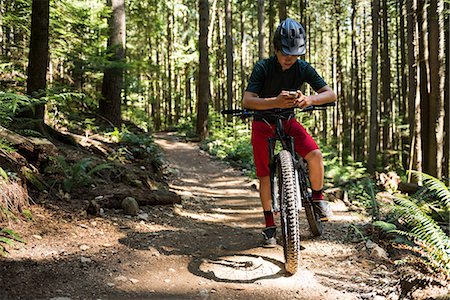 Male cyclist using mobile phone in forest on a sunny day Stock Photo - Premium Royalty-Free, Code: 6109-08764777