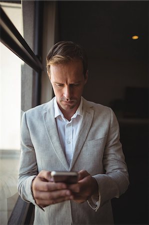 simsearch:6109-06685044,k - Pensive businessman using his mobile phone near the window in office Stock Photo - Premium Royalty-Free, Code: 6109-08765096