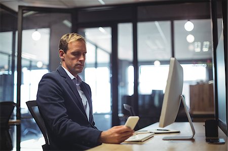 simsearch:6109-06685044,k - Businessman using mobile phone while sitting at desk in office Stock Photo - Premium Royalty-Free, Code: 6109-08765139