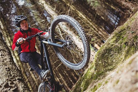 Low angle view of male biker jumping with bicycle in woodland Stock Photo - Premium Royalty-Free, Code: 6109-08700556