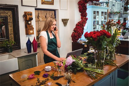 Female florist using laptop while talking on mobile phone in the flower shop Stock Photo - Premium Royalty-Free, Code: 6109-08700641