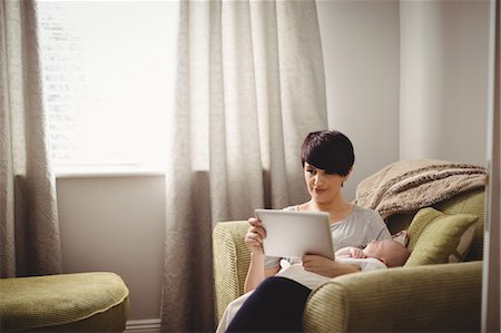 Mother using digital tablet while baby sleeping in her arm at living room Stock Photo - Premium Royalty-Free, Code: 6109-08700728