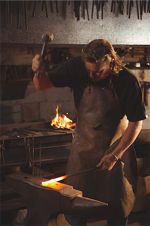 simsearch:400-06560568,k - Blacksmith working on hot metal using hammer to shape at work shop Photographie de stock - Premium Libres de Droits, Code: 6109-08700813