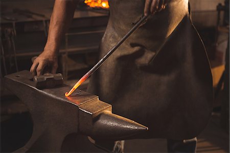 simsearch:400-06560568,k - Mid section blacksmith working on hot metal using hammer to shape at work shop Photographie de stock - Premium Libres de Droits, Code: 6109-08700814