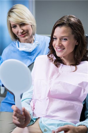 dentistry - Smiling patient looking in the mirror with a dentist sitting bed her Stock Photo - Premium Royalty-Free, Code: 6109-08700818