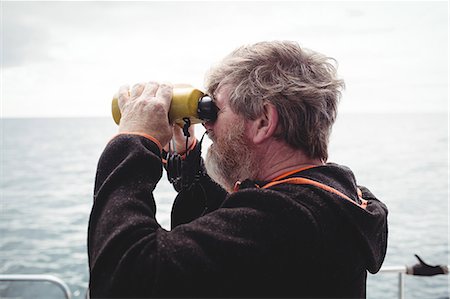 Fisherman looking through binoculars from boat Stock Photo - Premium Royalty-Free, Code: 6109-08701052