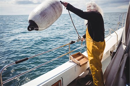 Fisherman throwing a buoy into the sea from fishing boat Foto de stock - Sin royalties Premium, Código: 6109-08701082