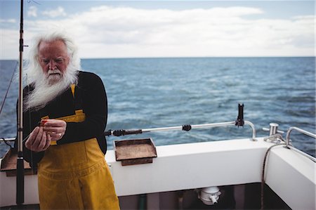 Fisherman preparing fishing rod on fishing boat Stock Photo - Premium Royalty-Free, Code: 6109-08701021