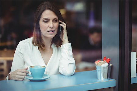 Woman holding coffee cup and talking on mobile phone in cafeteria Stock Photo - Premium Royalty-Free, Code: 6109-08701363