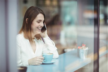 simsearch:6109-08690411,k - Woman holding coffee cup and talking on mobile phone in cafeteria Stock Photo - Premium Royalty-Free, Code: 6109-08701377