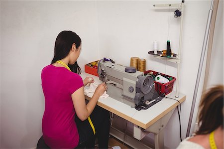 simsearch:6109-08701535,k - Female dressmaker sewing on the sewing machine in the studio Stock Photo - Premium Royalty-Free, Code: 6109-08701548