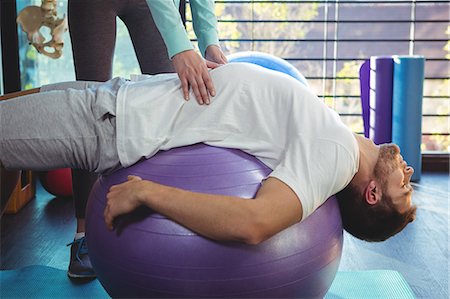 physiotherapy - Female physiotherapist helping male patient on exercise ball in the clinic Stock Photo - Premium Royalty-Free, Code: 6109-08701735