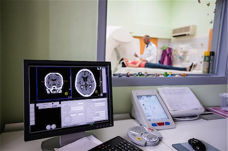 doctors talking to patients - Digital brain scan on computer monitor with MRI scanner in background Stock Photo - Premium Royalty-Free, Code: 6109-08720112