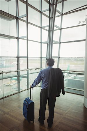 simsearch:400-03938985,k - Rear view of businessman with luggage looking through glass window at airport Foto de stock - Sin royalties Premium, Código: 6109-08722641