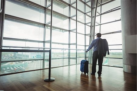 simsearch:400-03938985,k - Rear view of businessman with luggage looking through glass window at airport Foto de stock - Sin royalties Premium, Código: 6109-08722642