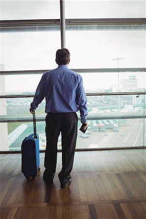 simsearch:400-03938985,k - Rear view of businessman with luggage looking through glass window at airport Foto de stock - Sin royalties Premium, Código: 6109-08722646