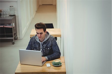 simsearch:6109-08690411,k - Man using laptop with coffee cup on table in coffee shop Stock Photo - Premium Royalty-Free, Code: 6109-08802068