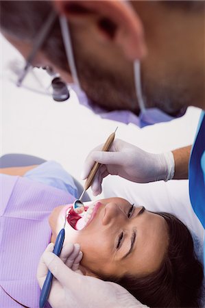 dentist with patient in exam room - Dentist examining a female patient with tools at dental clinic 4k Stock Photo - Premium Royalty-Free, Code: 6109-08803942