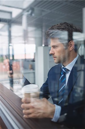simsearch:6109-08700458,k - Businessman using mobile phone and holding disposable coffee cup in office Stock Photo - Premium Royalty-Free, Code: 6109-08804211