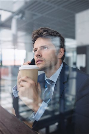 simsearch:6109-08700458,k - Businessman using mobile phone and holding disposable coffee cup in office Stock Photo - Premium Royalty-Free, Code: 6109-08804220