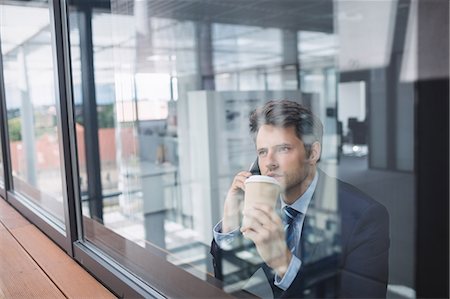 simsearch:6109-08700458,k - Businessman using mobile phone and holding disposable coffee cup in office Stock Photo - Premium Royalty-Free, Code: 6109-08804227