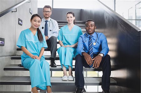 simsearch:6109-08804356,k - Portrait of smiling doctors and nurses sitting on staircase in hospital Stock Photo - Premium Royalty-Free, Code: 6109-08804353