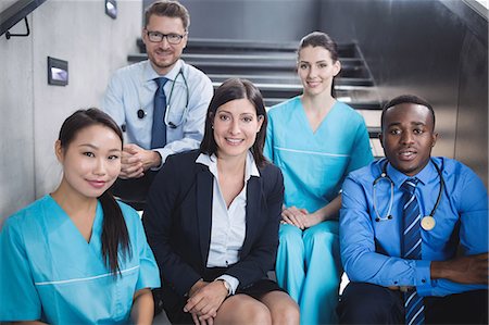 simsearch:6109-08804356,k - Portrait of smiling doctors and nurses sitting on staircase in hospital Stock Photo - Premium Royalty-Free, Code: 6109-08804354