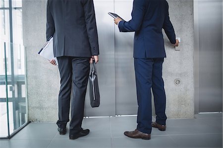 simsearch:6109-06684997,k - Low section of businessmen standing by lift and pressing button in office Stock Photo - Premium Royalty-Free, Code: 6109-08804458