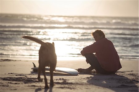 sit man dog - Man with surfboard sitting on beach at dusk with his dog Stock Photo - Premium Royalty-Free, Code: 6109-08804524