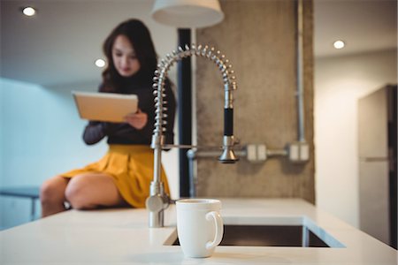 Woman sitting on kitchen worktop using digital tablet at home Stock Photo - Premium Royalty-Free, Code: 6109-08804746