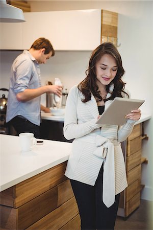 Woman using digital tablet while man working in background at kitchen Stock Photo - Premium Royalty-Free, Code: 6109-08804791