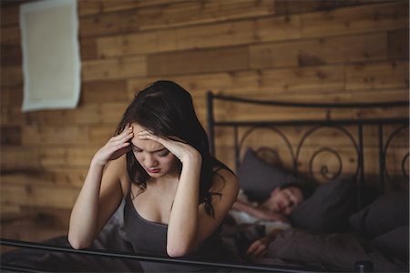simsearch:6109-07601529,k - Upset woman sitting on a bed while man sleeping in background at bedroom Stock Photo - Premium Royalty-Free, Code: 6109-08804833