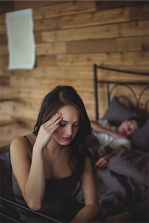 simsearch:6109-07601529,k - Upset woman sitting on a bed while man sleeping in background at bedroom Stock Photo - Premium Royalty-Free, Code: 6109-08804834