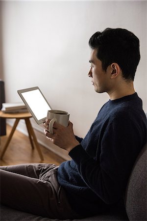 Man using digital tablet while having coffee at home Stock Photo - Premium Royalty-Free, Code: 6109-08804906