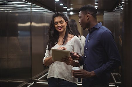 Businessman and a colleague discussing over digital tablet and mobile phone in office elevator Stock Photo - Premium Royalty-Free, Code: 6109-08805052