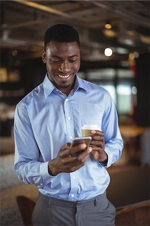 Businessman holding disposable coffee cup and using mobile phone in office Stock Photo - Premium Royalty-Free, Code: 6109-08805144