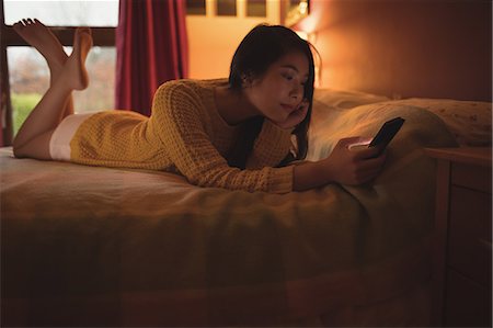 simsearch:845-05838374,k - Woman lying and using mobile phone on bed in bedroom at home Stock Photo - Premium Royalty-Free, Code: 6109-08944394
